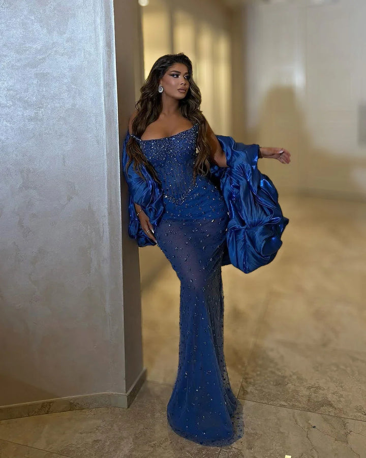 Full-length royal blue crystal corset mermaid gown with dramatic sculptural satin wrap at the arms