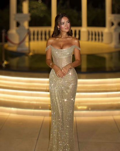 Full-length champagne crystal corset evening gown with draped off-shoulder neckline on illuminated steps