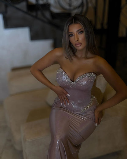 Kristal kenarlı kalp yakalı, heykelsi belli ve drapeli kalçalı gümüş eflatun metalik straplez korseli elbisenin oturarak görünümü